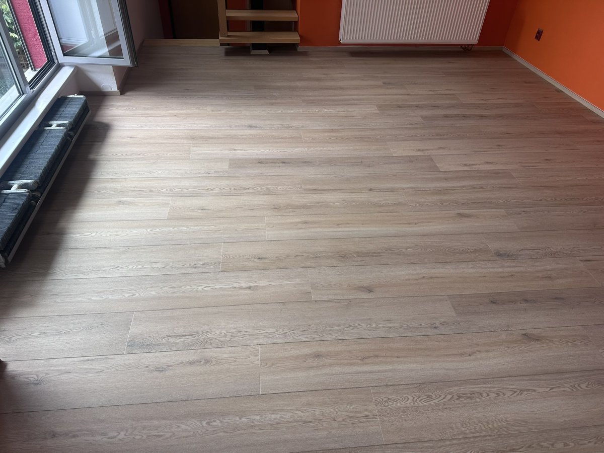 Prostorný obývací pokoj s nově lepenou zámkovou vinylovou podlahou v dekoru dubu u okna