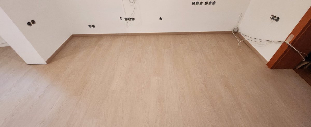 Detail nové vinylové podlahy taupe se soklovou lištou u stěny