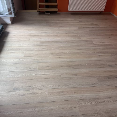 Prostorný obývací pokoj s nově lepenou zámkovou vinylovou podlahou v dekoru dubu u okna