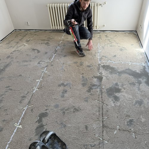 Řemeslník injektuje epoxidovou pryskyřici do trhlin v betonovém potěru před pokládkou vinylu